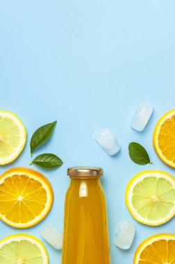Düz kompozisyon, cam meyve suyu şişeleri ya da taze, taze limon ve portakal dilimleri, yeşil yapraklar, buz küpleri mavi arkaplan manzaralı fotokopi alanı. Citrus meyve suyu konsepti, C vitamini, meyveler.