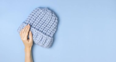 Düz mavi örülmüş kış şapkası mavi arka plan görünümlü kadınların elinde yatıyordu. Havalı yün şapka, soğuk için kış aksesuarları konsepti. Reklam, alışveriş, kış indirimi.