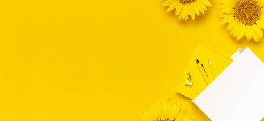 Çalışma masasının en üstteki düz yatağı ayçiçekli tasarım, beyaz kese kağıdı kalem kalem kalem kalem kalem günlük ataçları sarı arka planda. Sonbahar veya yaz konsepti. Ayçiçeği doğal arka plan