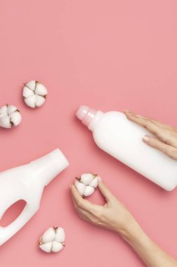 Çevre temizliği konsepti. Kadınların ellerinde beyaz plastik çamaşır deterjanı, sıvı tozu, çamaşır deterjanı, pembe arka planda pamuk çiçekleri var. Düz manzaralı. Biyo organik ürün