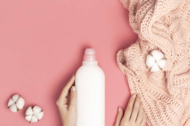 Çevre temizliği konsepti. Kadınların ellerinde beyaz plastik çamaşır deterjanı, sıvı tozu, çamaşır deterjanı, pembe arka planda pamuk çiçekleri var. Düz manzaralı. Biyo organik ürün
