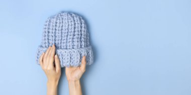 Düz mavi örülmüş kış şapkası mavi arka plan görünümlü kadınların elinde yatıyordu. Havalı yün şapka, soğuk için kış aksesuarları konsepti. Reklam, alışveriş, kış indirimi.