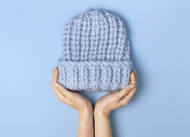 Düz mavi örülmüş kış şapkası mavi arka plan görünümlü kadınların elinde yatıyordu. Havalı yün şapka, soğuk için kış aksesuarları konsepti. Reklam, alışveriş, kış indirimi.