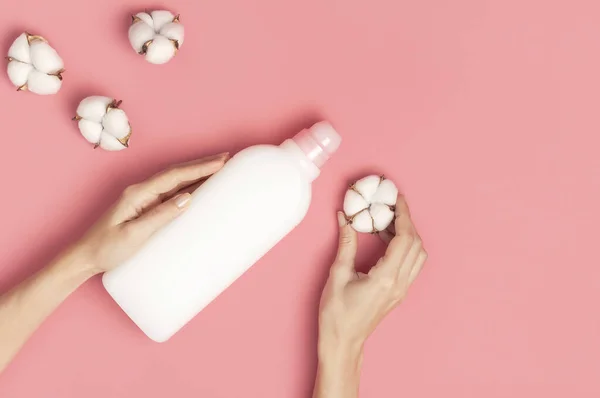 Eco cleaning concept. Women\'s hands hold white plastic packaging of laundry detergent, liquid powder, washing conditioner, cotton flowers on pink background. Flat lay top view. Bio organic product