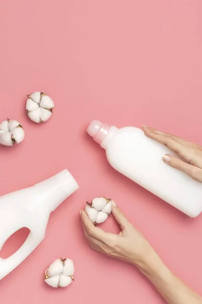 Eco cleaning concept. Women's hands hold white plastic packaging of laundry detergent, liquid powder, washing conditioner, cotton flowers on pink background. Flat lay top view. Bio organic product — Stock Photo, Image