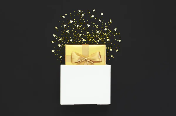 Regalo dorado con cinta de bolsa de papel blanco, estrellas de confeti sobre fondo negro. Piso tendido, vista superior, espacio para copiar. Decoraciones doradas, fiesta, cumpleaños, concepto de vacaciones. Año Nuevo Composición de Navidad — Foto de Stock