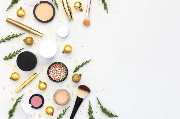 Makeup mascara foundation cream lipstick eyeshadow blush balls and New Year decorations gold Christmas balls confetti stars fir branches on light background Flat lay top view. Cosmetics, holiday Xmas