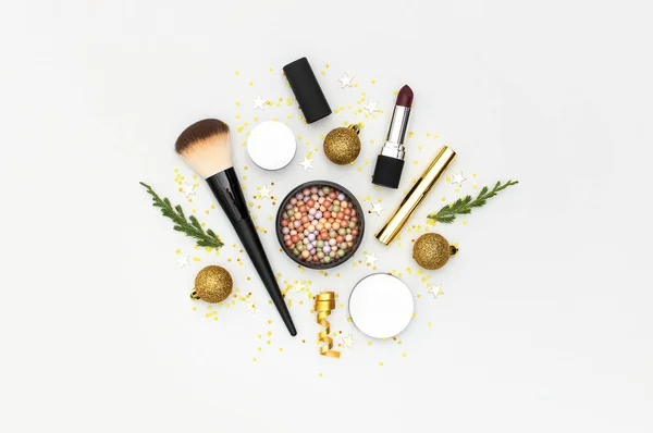 Makeup mascara foundation cream lipstick eyeshadow blush balls and New Year decorations gold Christmas balls confetti stars fir branches on light background Flat lay top view. Cosmetics, holiday Xmas