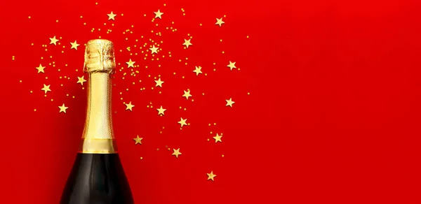 Natale e Capodanno sfondo. Bottiglia di champagne, festivi coriandoli stellati dorati su sfondo rosso vista dall'alto. Biglietto per vacanze flat lay. Concetto di compleanno o matrimonio. Decorazioni festive 2020 Natale — Foto Stock