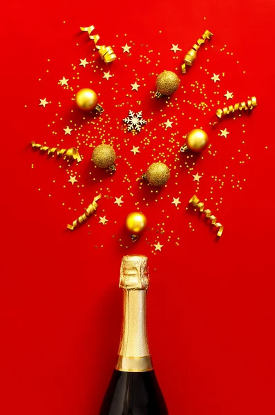 Święta i Nowy Rok. Butelka szampana, złote kulki świąteczne, świąteczne wstążki, gałązki jodły, konfetti gwiazdkowe na czerwonym tle widok z góry. Płaska karta wakacyjna. Uroczyste dekoracje 2020 — Zdjęcie stockowe