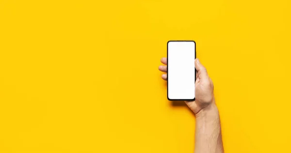 Férfi kéz tart egy modern fekete okostelefon fehér üres képernyő sárga háttér. Modern technológia, telefon, szerkentyű a kezében, érintőképernyő, sablon a design. Mockup — Stock Fotó