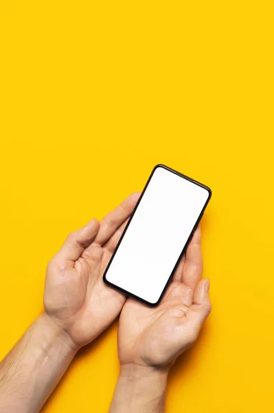 Чоловічі руки тримають сучасний чорний смартфон з білим порожнім екраном на жовтому тлі. Сучасні технології, телефон, гаджет в руках, сенсорний екран, шаблон вашого дизайну. Мокап — стокове фото
