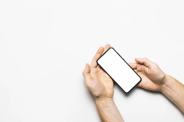 Чоловічі руки тримають сучасний чорний смартфон з білим порожнім екраном на світло-сірому тлі. Сучасні технології, телефон, гаджет в руках, сенсорний екран, шаблон вашого дизайну. Мокап — стокове фото