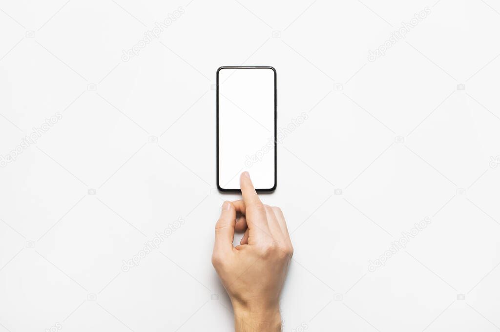Male hands hold a modern black smartphone with white blank screen on light gray background. Modern technology, phone, gadget in hands, touch screen, template for your design. Mockup