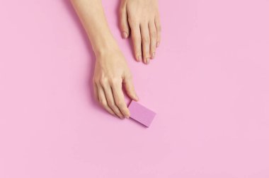 Güzel, zarif bir manikür. Pembe arka planda tırnak törpüsü olan genç bir kadının elleri düz fotokopi alanında yatıyor. Doğal oje, jöle, kişisel bakım, güzellik ve moda. Manikür salonu spası.