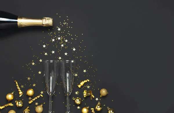 Christmas and New Year background. Champagne bottle champagne glasses golden christmas balls festive ribbons star confetti on black background top view. Flat lay holiday card. Party decorations 2020