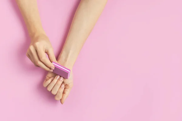 Κομψό όμορφο απαλό μανικιούρ. Χέρια της νεαρής γυναίκας με καρφί αρχείο σε ροζ φόντο πάνω άποψη επίπεδη lay αντίγραφο χώρο. Φυσικά νύχια, βερνίκι τζελ, αυτοφροντίδα, ομορφιά και μόδα. Σαλόνι περιποίησης νυχιών — Φωτογραφία Αρχείου