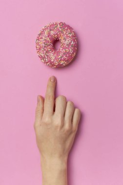 Beautiful female hands with gentle manicure hold sweet donut on pink background top view flat lay copy space. Natural nails, gel polish, self-care, beauty and fashion. Nail care. Donut Background
