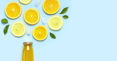 Düz kompozisyon, cam meyve suyu şişeleri ya da taze, taze limon ve portakal dilimleri, yeşil yapraklar, buz küpleri mavi arkaplan manzaralı fotokopi alanı. Citrus meyve suyu konsepti, C vitamini, meyveler.