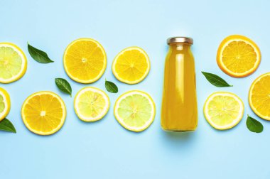 Düz kompozisyon, cam meyve suyu şişeleri ya da taze, taze limon ve portakal dilimleri, yeşil yapraklar, buz küpleri mavi arkaplan manzaralı fotokopi alanı. Citrus meyve suyu konsepti, C vitamini, meyveler.