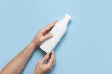 Süt ürünleri için beyaz plastik şişeler erkeklerin elinde mavi arka plan manzaralı düz yerde. Plastik Kefir Yoğurt Şişe Sütü. Paketleme şablonu modeli. Tasarımınız için düzenName