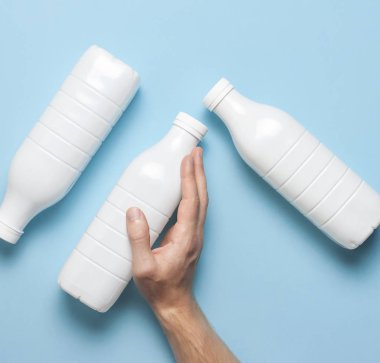 Süt ürünleri için beyaz plastik şişeler erkeklerin elinde mavi arka plan manzaralı düz yerde. Plastik Kefir Yoğurt Şişe Sütü. Paketleme şablonu modeli. Tasarımınız için düzenName