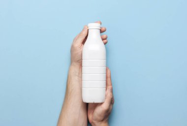 Süt ürünleri için beyaz plastik şişeler erkeklerin elinde mavi arka plan manzaralı düz yerde. Plastik Kefir Yoğurt Şişe Sütü. Paketleme şablonu modeli. Tasarımınız için düzenName