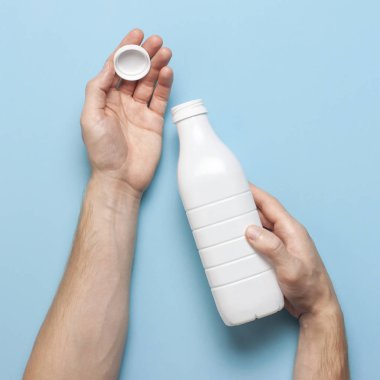Süt ürünleri için beyaz plastik şişeler erkeklerin elinde mavi arka plan manzaralı düz yerde. Plastik Kefir Yoğurt Şişe Sütü. Paketleme şablonu modeli. Tasarımınız için düzenName