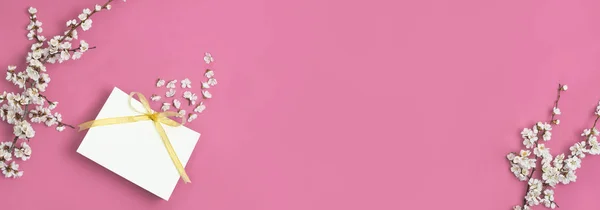 Saco de presente branco com fita de ouro e ramo de flores brancas de primavera em fundo rosa brilhante. Cartão de saudação com flores delicadas Fundo floral rosa. Conceito mínimo de primavera. Flat lay vista superior — Fotografia de Stock