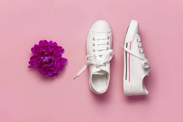 White female fashion sneakers and pink purple flowers peonies on pink background. Flat lay top view copy space. Women's shoes. Stylish white sneakers. Fashion blog or magazine. Spring shoe concept — Stock Photo, Image