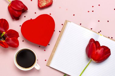 Red tulips, red heart shaped gift box, cup of coffee, blank notebook, macaron cake, confetti on pastel pink background top view Flat lay. Mother's Day Valentines Day birthday holiday background