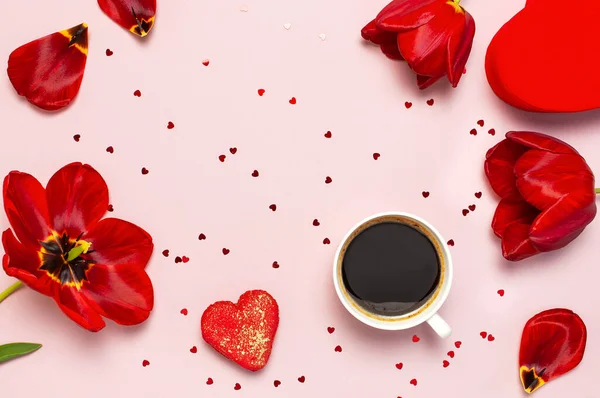 Kırmızı laleler, kırmızı kalp şeklinde hediye kutusu, kahve fincanı, makarna kek, pastel pembe arka plan üst görünümü Düz konfeti yatıyordu. Anneler Günü Sevgililer Günü doğum günü tatil arka plan. Güzel tebrik kartı