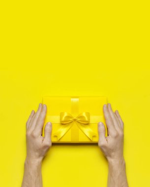Erkek eller, sarı arka plan manzaralı parlak sarı hediye kutusunu tutuyor. Tatil geçmişi düzdü. Doğum günü hediyesi, 8 Mart, Anneler Günü, Sevgililer Günü. Tebrikler.
