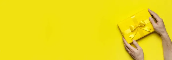 Mężczyzna ręce gospodarstwa jasnożółty prezent prezent pudełko z wstążką na żółtym tle widok z góry. Płaskie tło wakacyjne. Prezent urodzinowy 8 marca, Dzień Matki, Walentynki. Gratuluję. — Zdjęcie stockowe