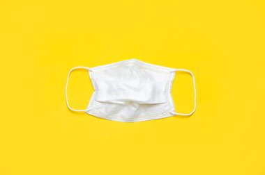 Sarı arka plandaki tıbbi maske düz bir şekilde fotokopi alanının üstünde duruyordu. Virüse karşı koruma, koronavirüs, grip, soğuk algınlığı, hastalıklar. Geleneksel tıbbi araç, sağlık kavramı. Tıbbi geçmiş