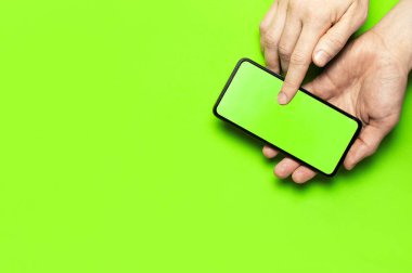 Erkek eller, neon yeşil arka plan düz manzaralı yeşil ekranlı modern siyah akıllı telefonu tutarlar. Modern teknoloji, telefon, cihazlar, dokunmatik ekran, tasarımınız için şablon. Model