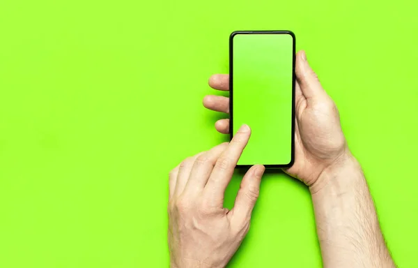Férfi kéz tart egy modern fekete okostelefon zöld üres képernyő neon zöld háttér lapos tetején nézet. Modern technológia, telefon, szerkentyű a kezében, érintőképernyő, sablon a design. Mockup — Stock Fotó