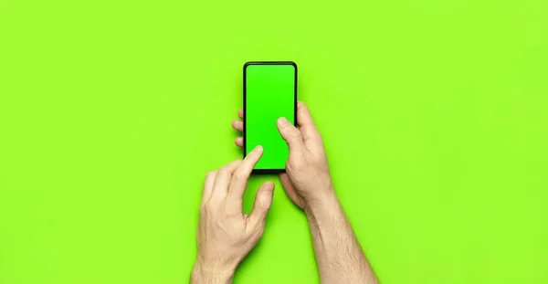 Чоловічі руки тримають сучасний чорний смартфон із зеленим порожнім екраном на неоновому зеленому фоні з плоским видом зверху. Сучасні технології, телефон, гаджет в руках, сенсорний екран, шаблон вашого дизайну. Мокап — стокове фото