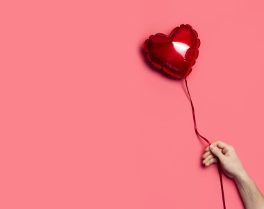 Aşk konsepti. Erkek el, pembe arka planda kalp şeklinde kırmızı bir balon tutuyor. Tatil Nesnesi, Doğum günü, Sevgililer Günü, Düğün. Parti dekorasyonu. Tebrik kartı