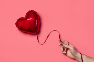 Aşk konsepti. Erkek el, pembe arka planda kalp şeklinde kırmızı bir balon tutuyor. Tatil Nesnesi, Doğum günü, Sevgililer Günü, Düğün. Parti dekorasyonu. Tebrik kartı