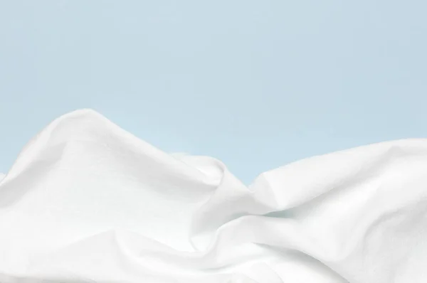 白色皱皱的天然棉织物在精致的蓝色背景上,顶部的视野平坦,有复制的空间.天然亚麻布背景。生态纺织品。白色面料质地。面料背景 — 图库照片