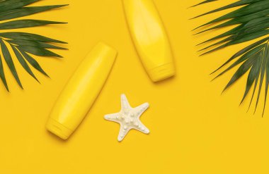 Sarı güneş kremi şişeleri, tropikal palmiye yaprakları, kabuklar, sarı arka planda deniz yıldızı düz görünüm alanı. Güneş koruması Yaz tatili seyahat konsepti Yaz kozmetiği.