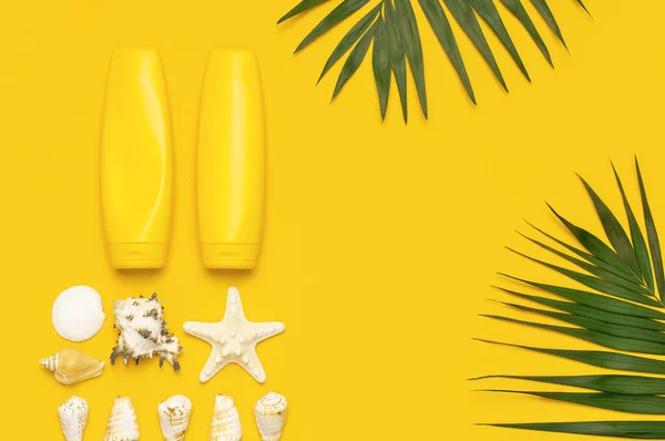 Yellow bottles of sunscreen cream, tropical palm leaves, shells, starfish on yellow background top view flat lay copy space. Sun protection Summer background vacation travel concept Summer cosmetics.