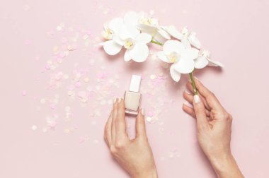 Pastel renklerde şık şık kadın manikür. Şenlikli konfeti ile pembe arka plan üzerinde oje şişesi tutan genç kızın elleri. Minimalist manikür trendi Düz lay top view kopya alanı.