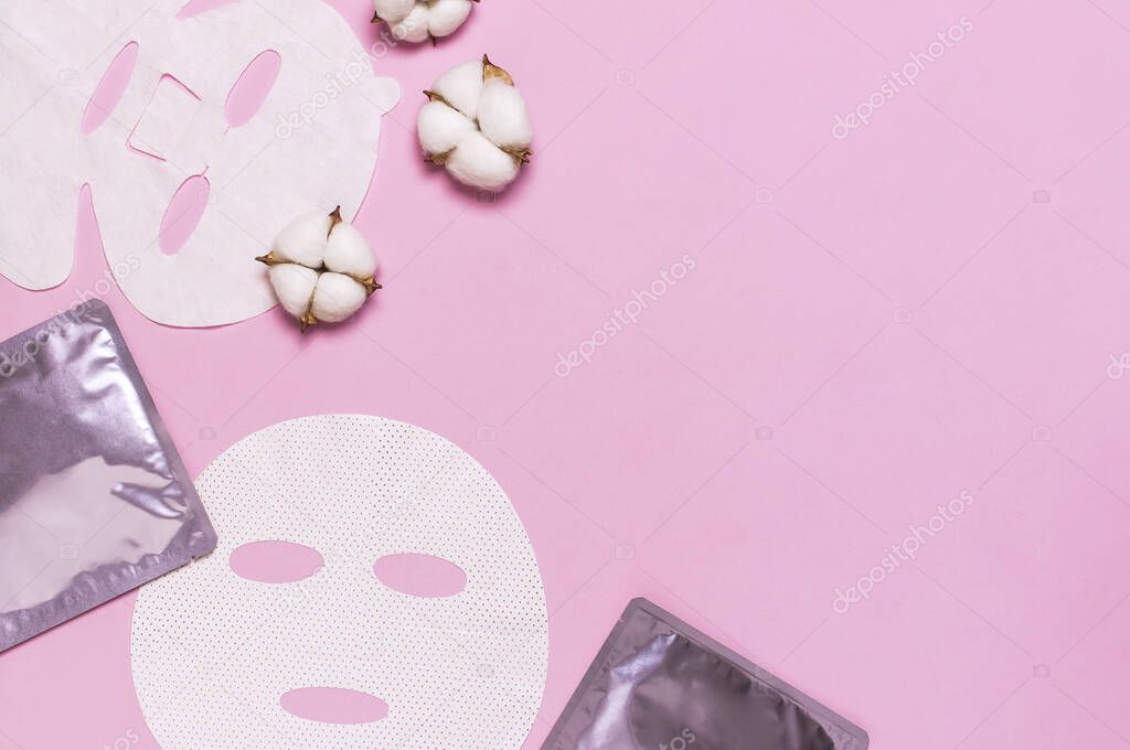 Fabric face mask, cotton flowers on pink background. Concept of natural cosmetics, face care, spa, face cream, women's beauty accessories. Flat lay top view copy space. Cosmetics mock-up.