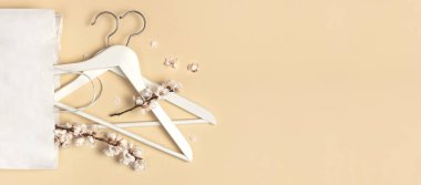 Yaratıcı bahar satışı konsepti. Bahar çiçekli beyaz ahşap askılar bej arka planda beyaz kağıt torba düz manzaralı. Moda bahar indirimleri mağaza tanıtım tasarımı minimalizm tarzını indiriyor.