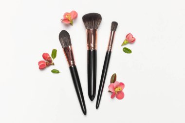 Açık gri arka plan üzerinde pembe bahar çiçekleri olan profesyonel makyaj fırçaları üst görünüm kopya alanı yatıyordu. Güzellik malzemesi, makyaj, kadın aksesuarı, moda. Makyaj seti.