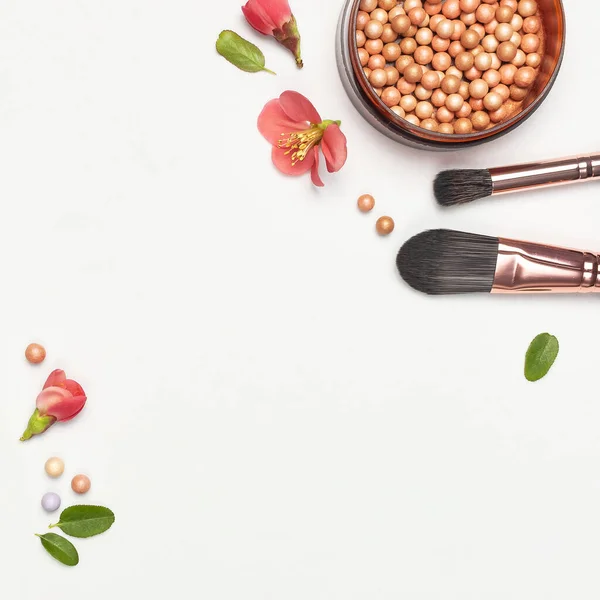 Professional makeup brushes powder blush balls with pink spring flowers on light background flat lay top view copy space. Beauty product, makeup, women's accessory, fashion. Cosmetic makeup Set.