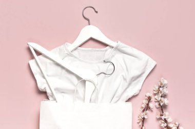 Yaratıcı bahar satışı konsepti. Beyaz ahşap askılar, bahar çiçekleri, pembe arka planda beyaz gömlek, kağıt torba düz zemin. Moda bahar indirimi mağaza tanıtım tasarımı.