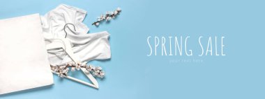 Creative spring sale concept. White wooden hangers with spring flowers white shirt paper bag on blue background top view flat lay. Fashion spring discounts shopping sale store promo design. clipart